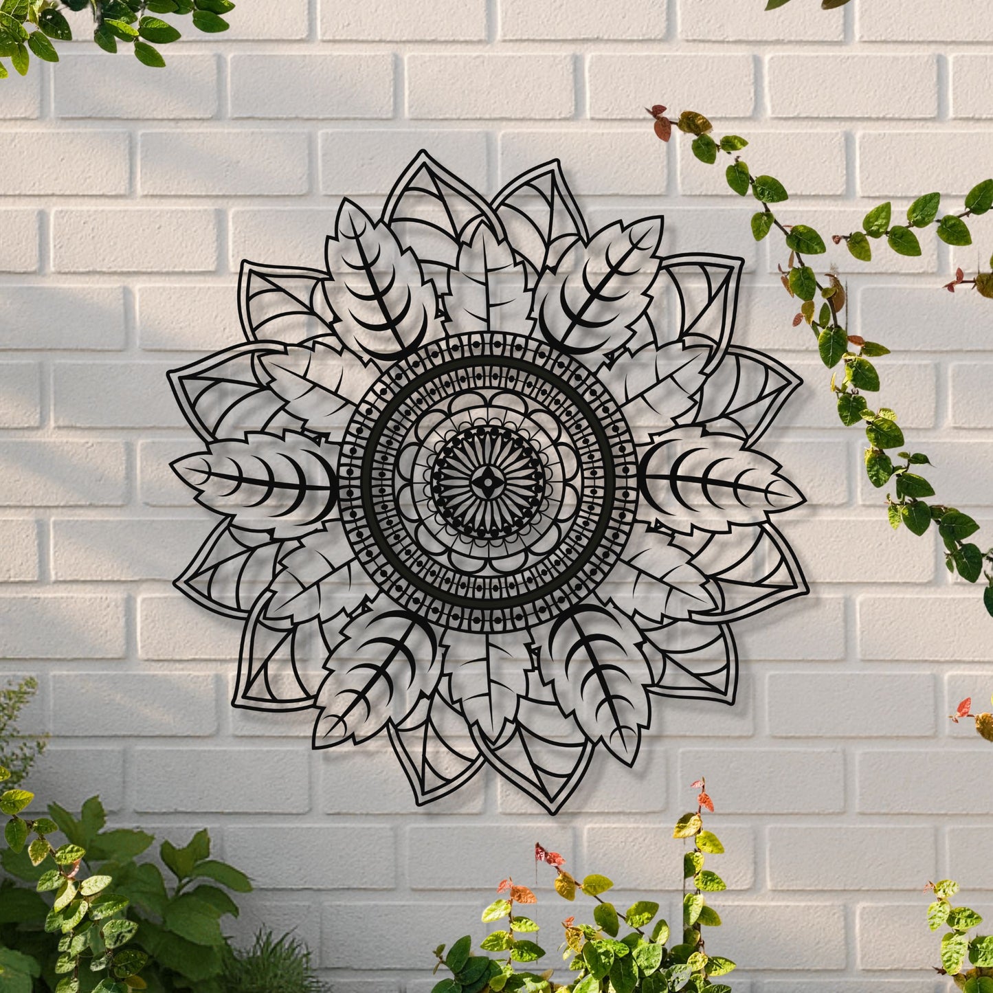 Decorative black mandala wall art on a white brick wall with greenery.