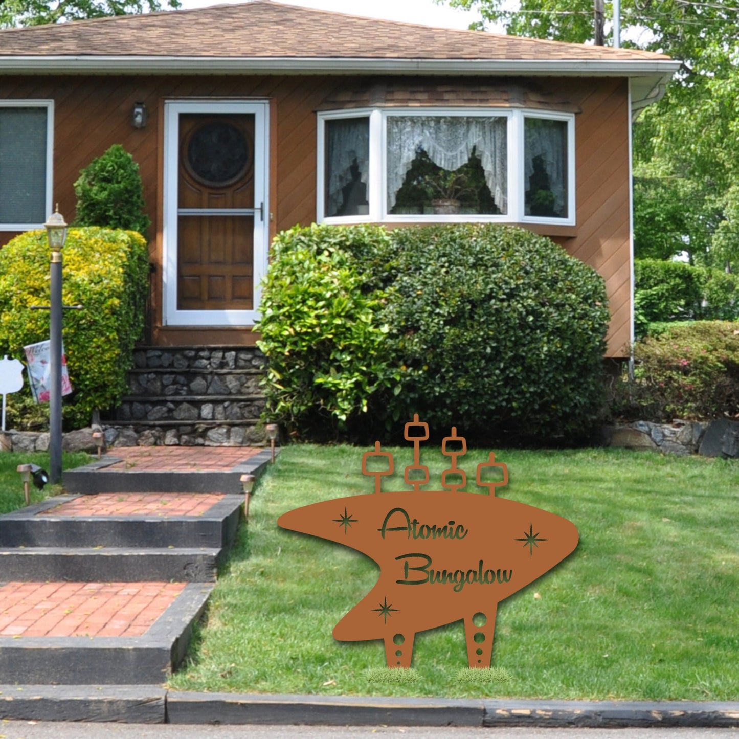 Decorative sign for 'Atomic Bungalow' in front of a house with greenery.