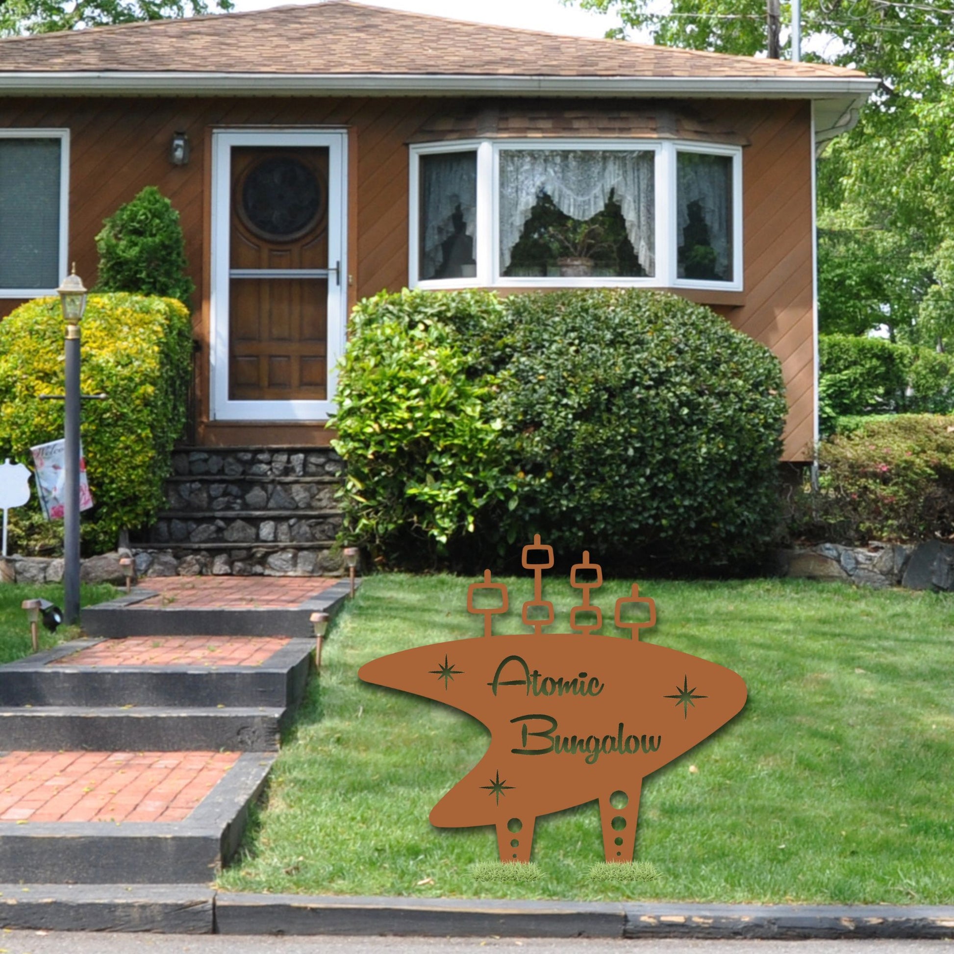 Decorative sign for 'Atomic Bungalow' in front of a house with greenery.