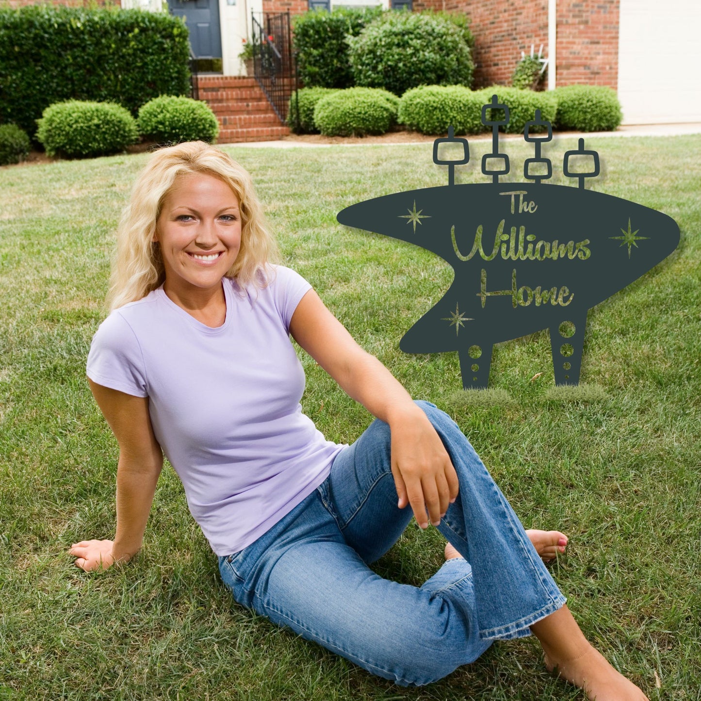 Woman sitting on grass with a personalized home sign in the background