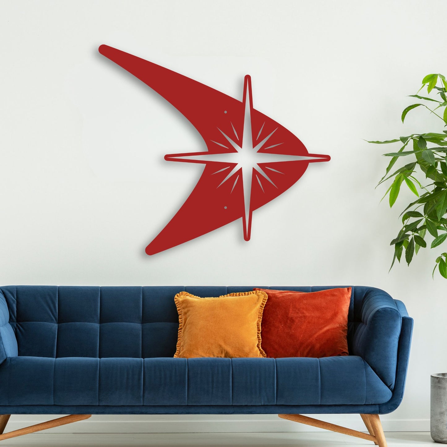 Red wall clock with white design on a white wall above a blue sofa with colorful cushions.