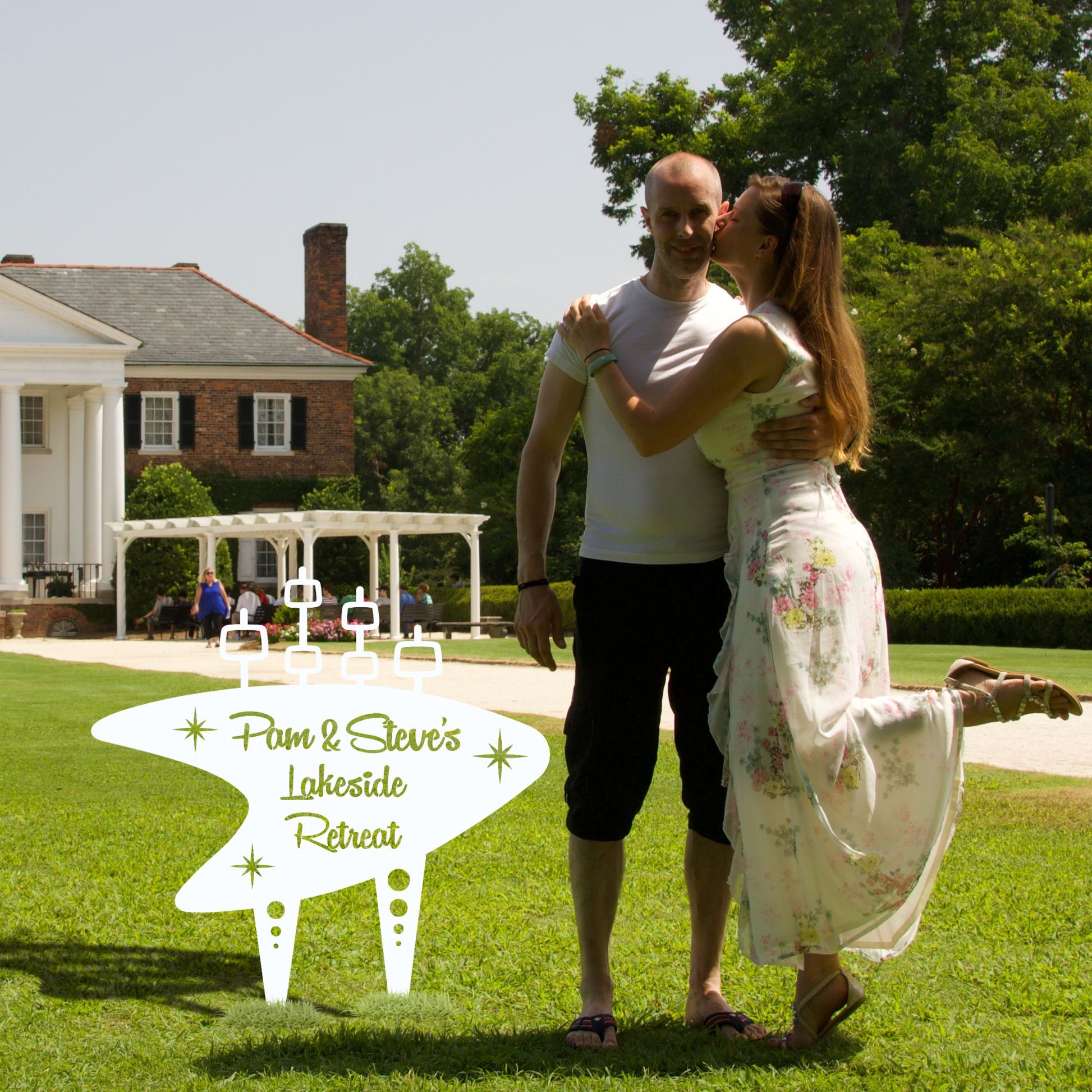 Couple embracing on a grassy lawn with a house and trees in the background, featuring 'Pam & Steve's Lakeside Retreat' text.