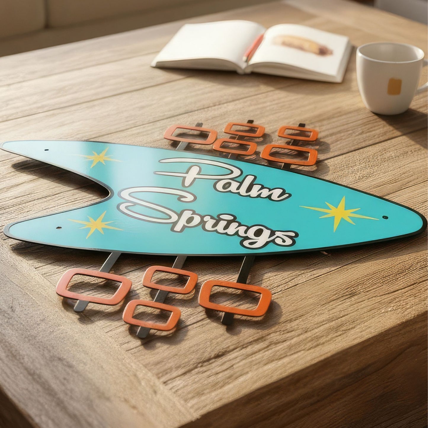Decorative sign with 'Palm Springs' text on a wooden surface with a book and mug in the background.