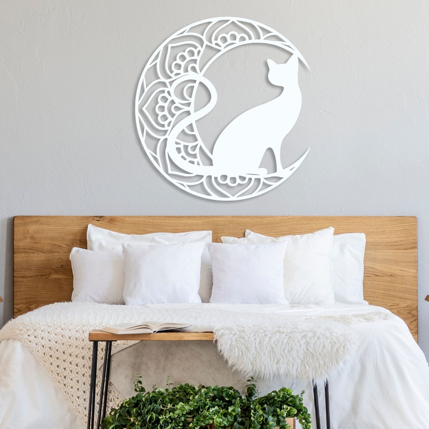 Decorative wall art of a cat in a crescent moon design above a bed with white bedding.