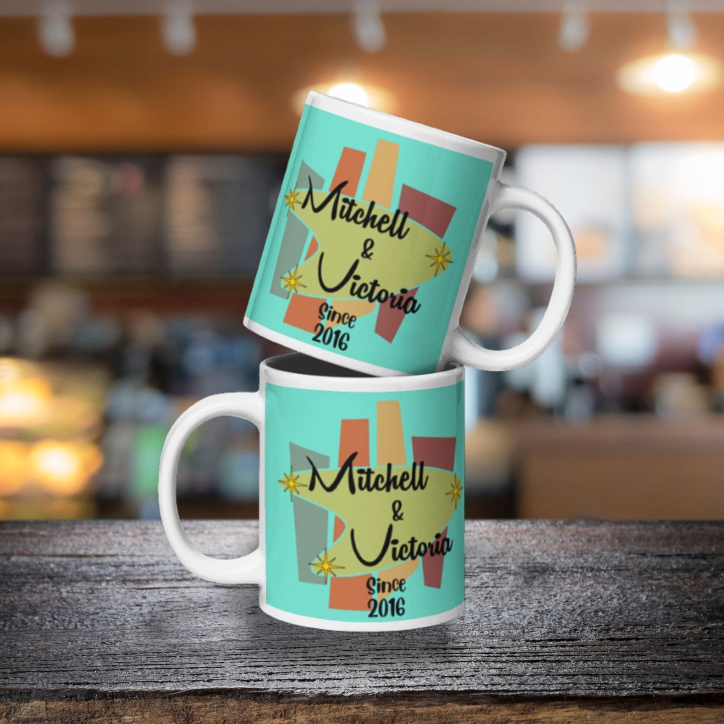 Two turquoise mugs with 'Mitchell & Victoria Since 2016' design on a wooden surface.