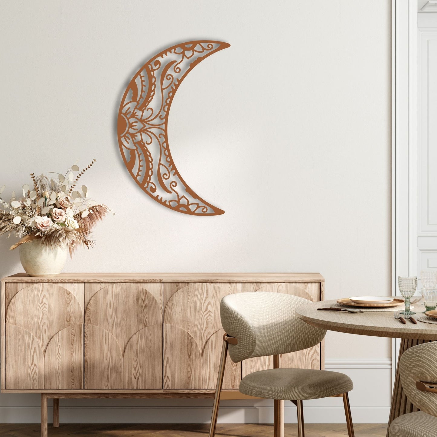 Decorative wall art in the shape of a crescent moon above a wooden sideboard with a vase of flowers.