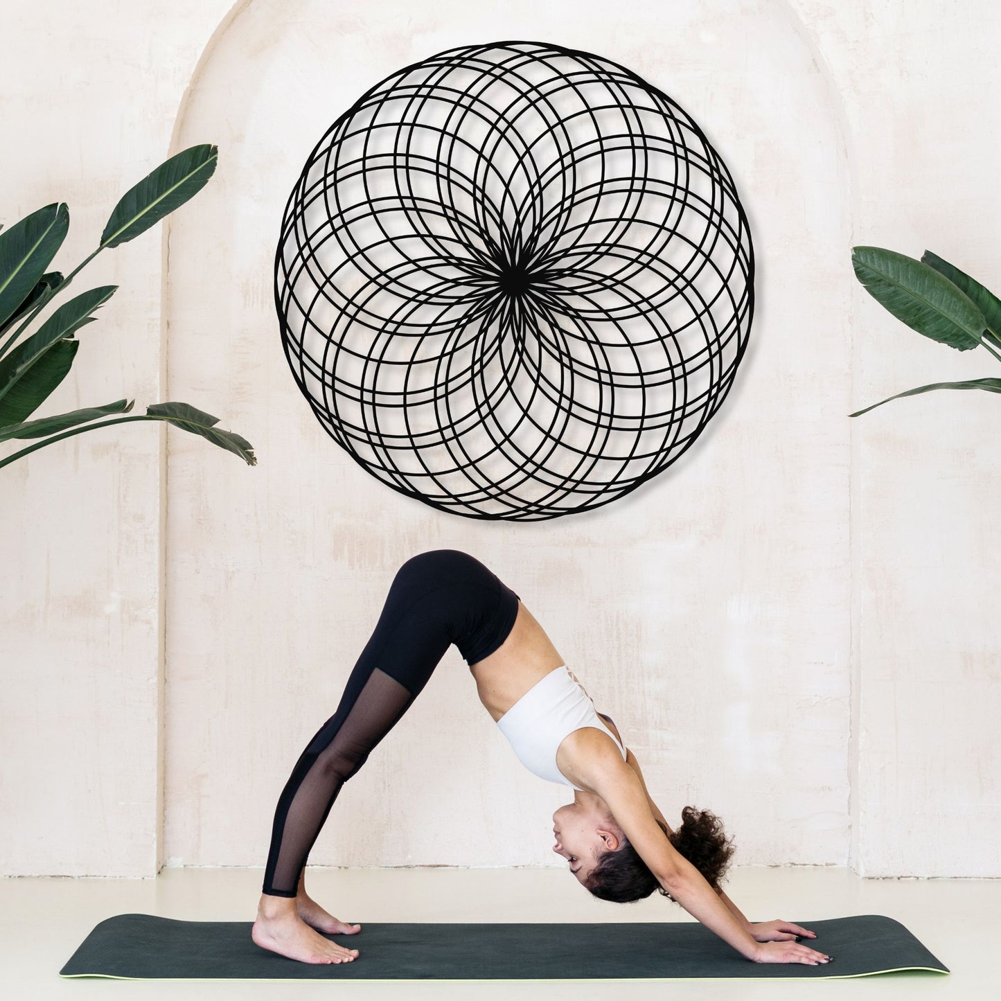 Person in a yoga pose on a mat with a decorative wall piece and plants in the background