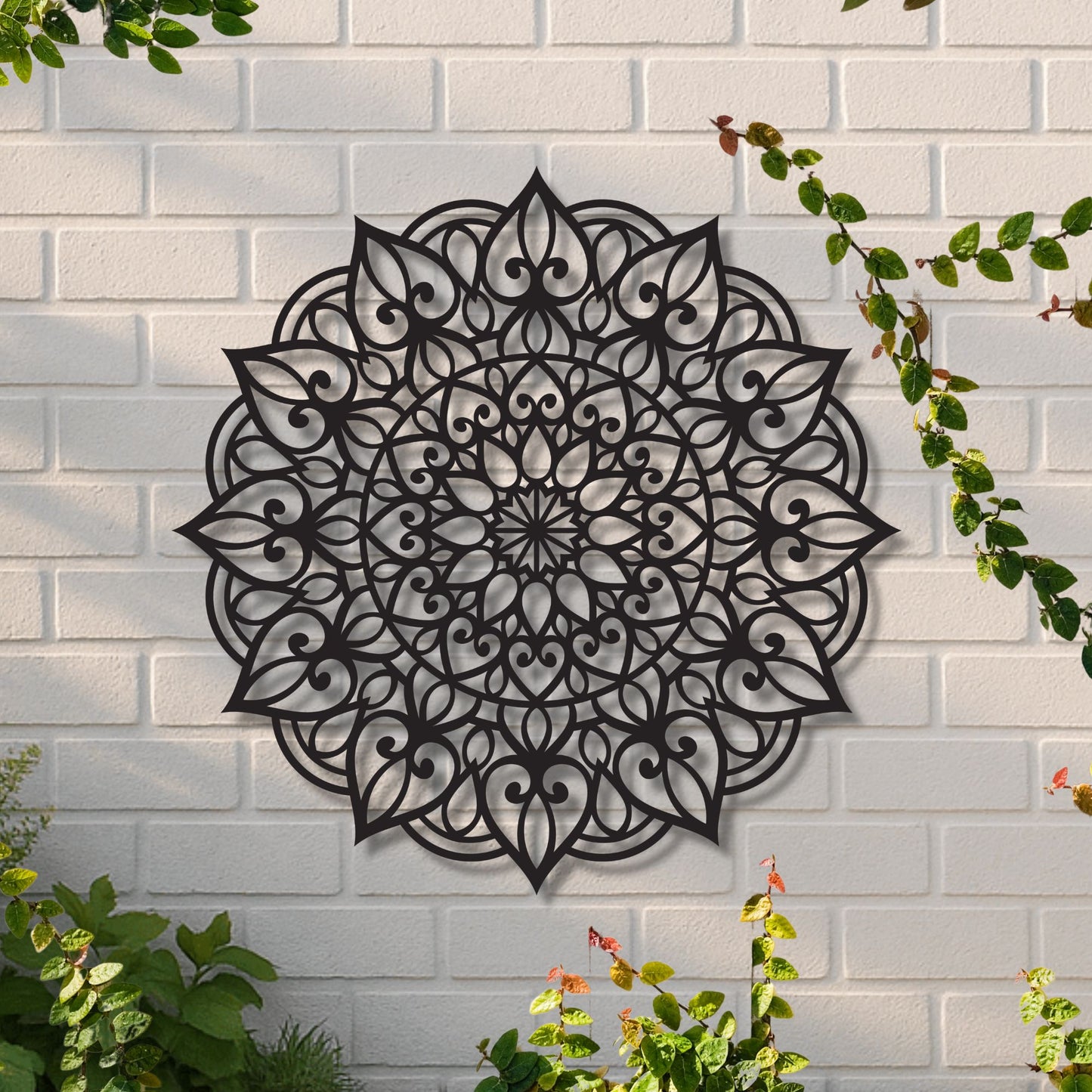 Decorative black mandala wall art on a white brick wall with greenery.