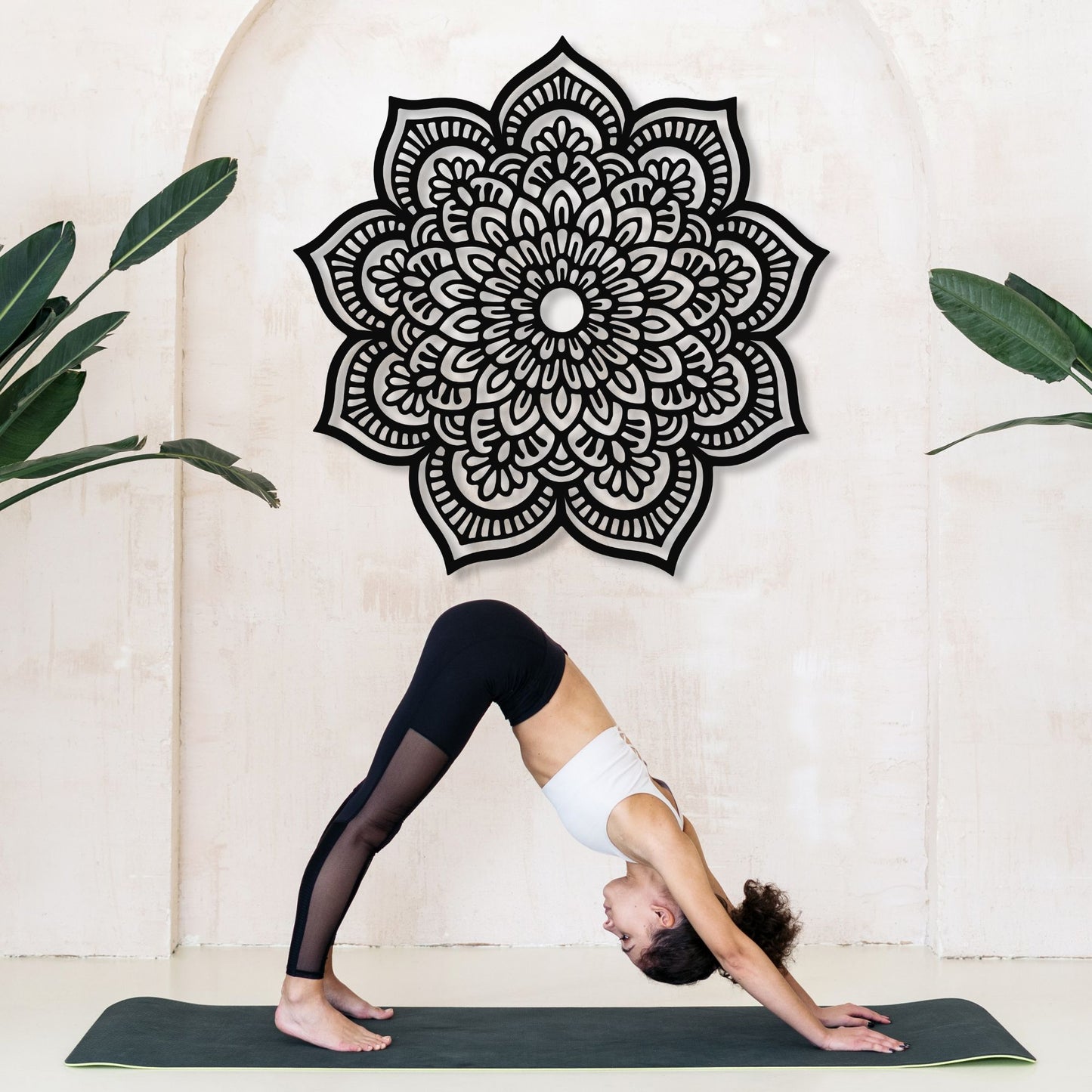 Person in a yoga pose on a mat with a decorative mandala wall art in the background.