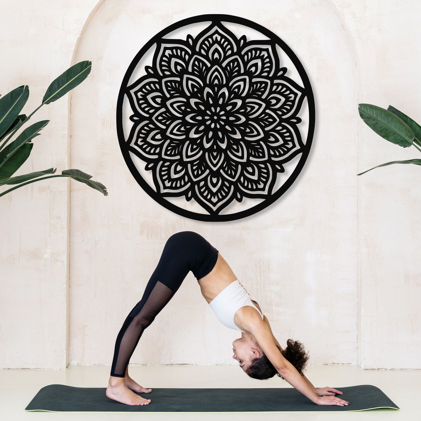 Person in a yoga pose on a mat with a decorative black mandala wall art in the background.