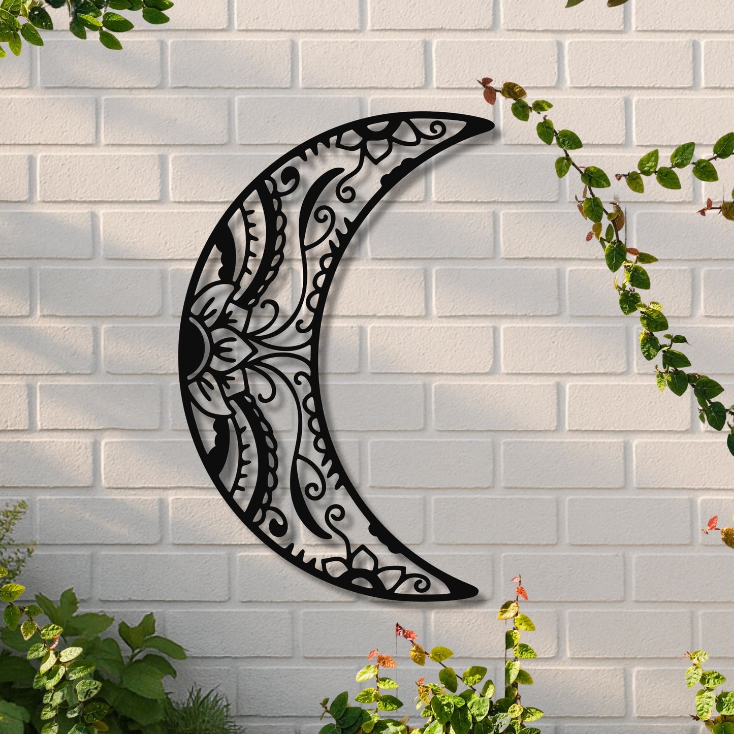 Decorative metal crescent moon wall art on a white brick wall with greenery.
