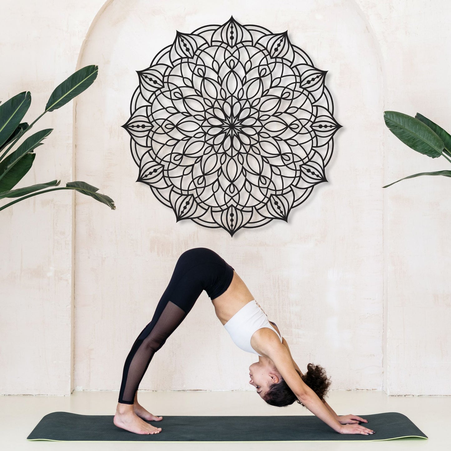 Person practicing yoga in a studio with a decorative wall mandala and plants.