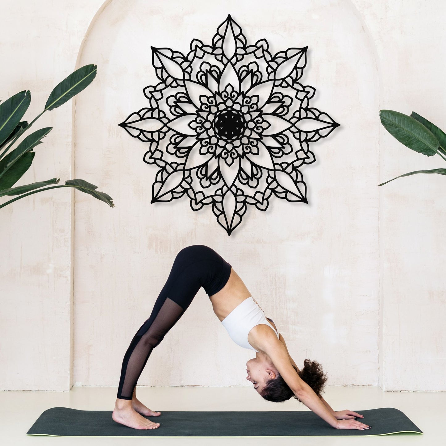 Person in a yoga pose on a mat with a decorative mandala wall art in the background.