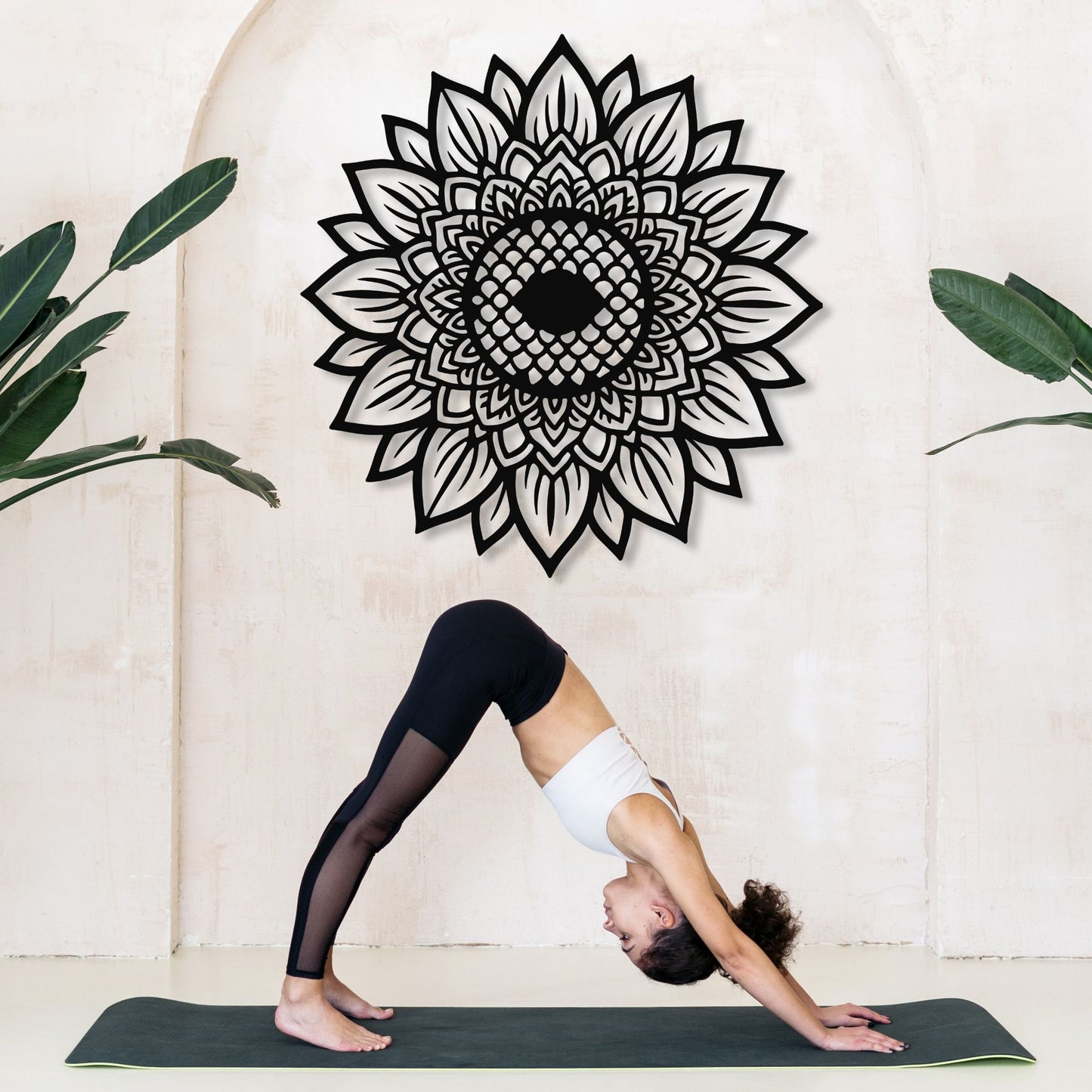 Person in a yoga pose on a mat with a decorative mandala wall art in the background.
