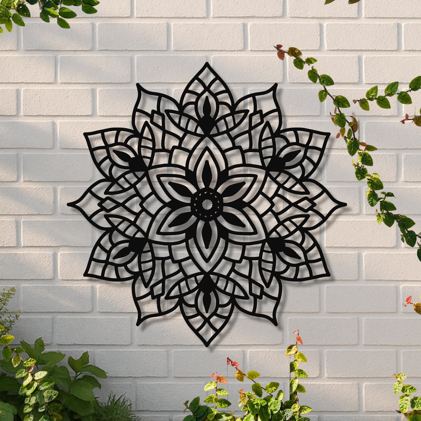 Decorative black metal wall art with floral pattern on a white brick wall.