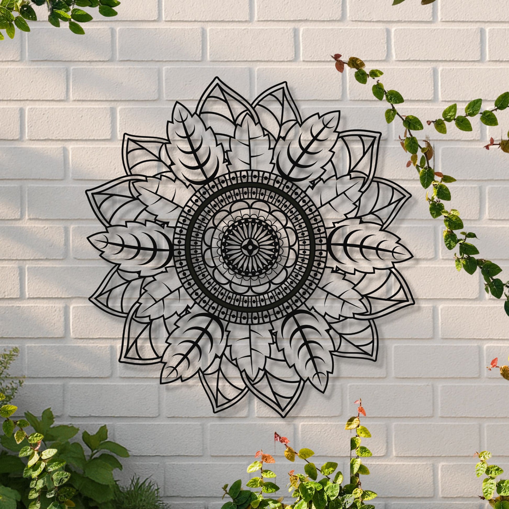 Decorative black mandala wall art on a white brick wall with greenery.