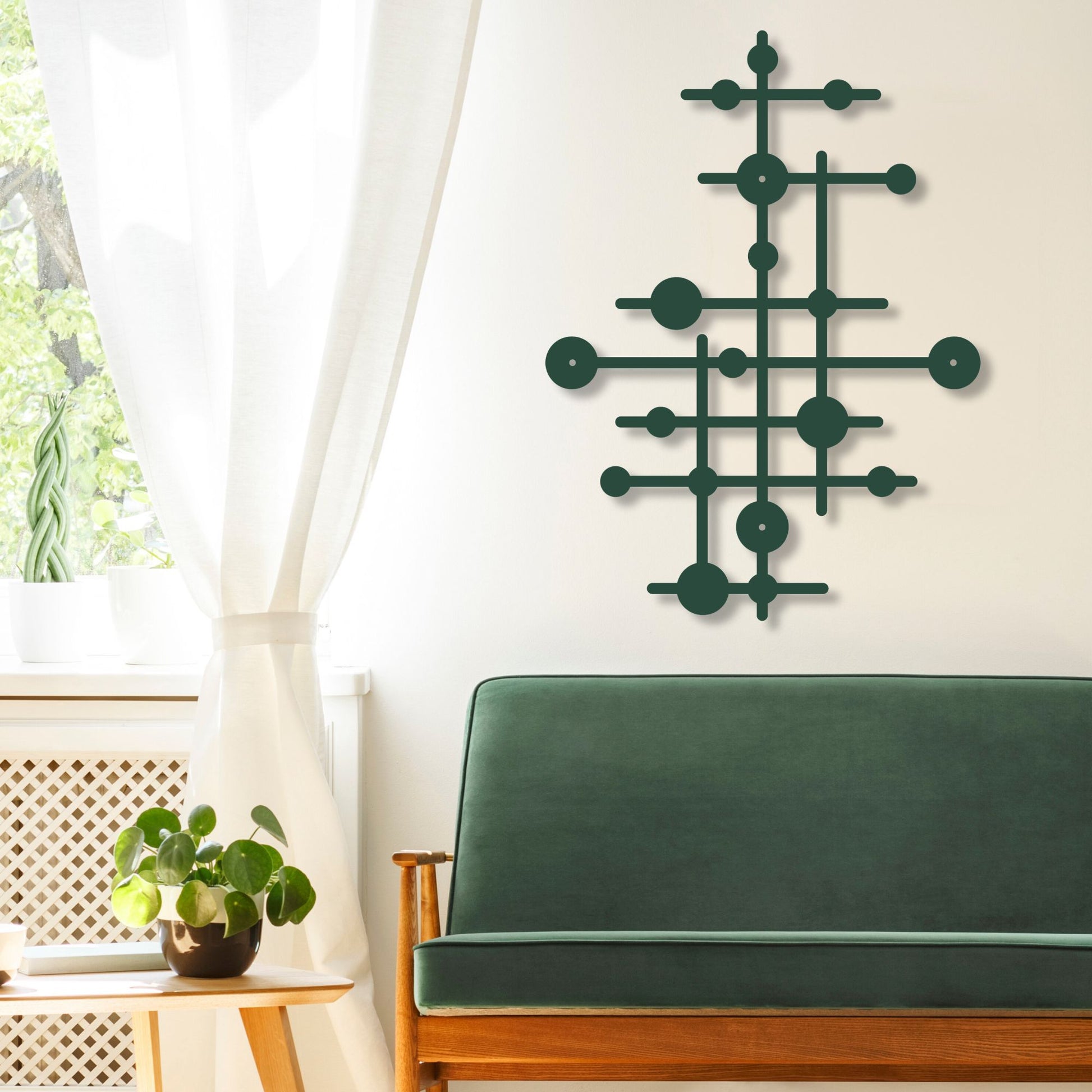 Geometric wall art on a white wall above a green sofa with a plant and window in the background.