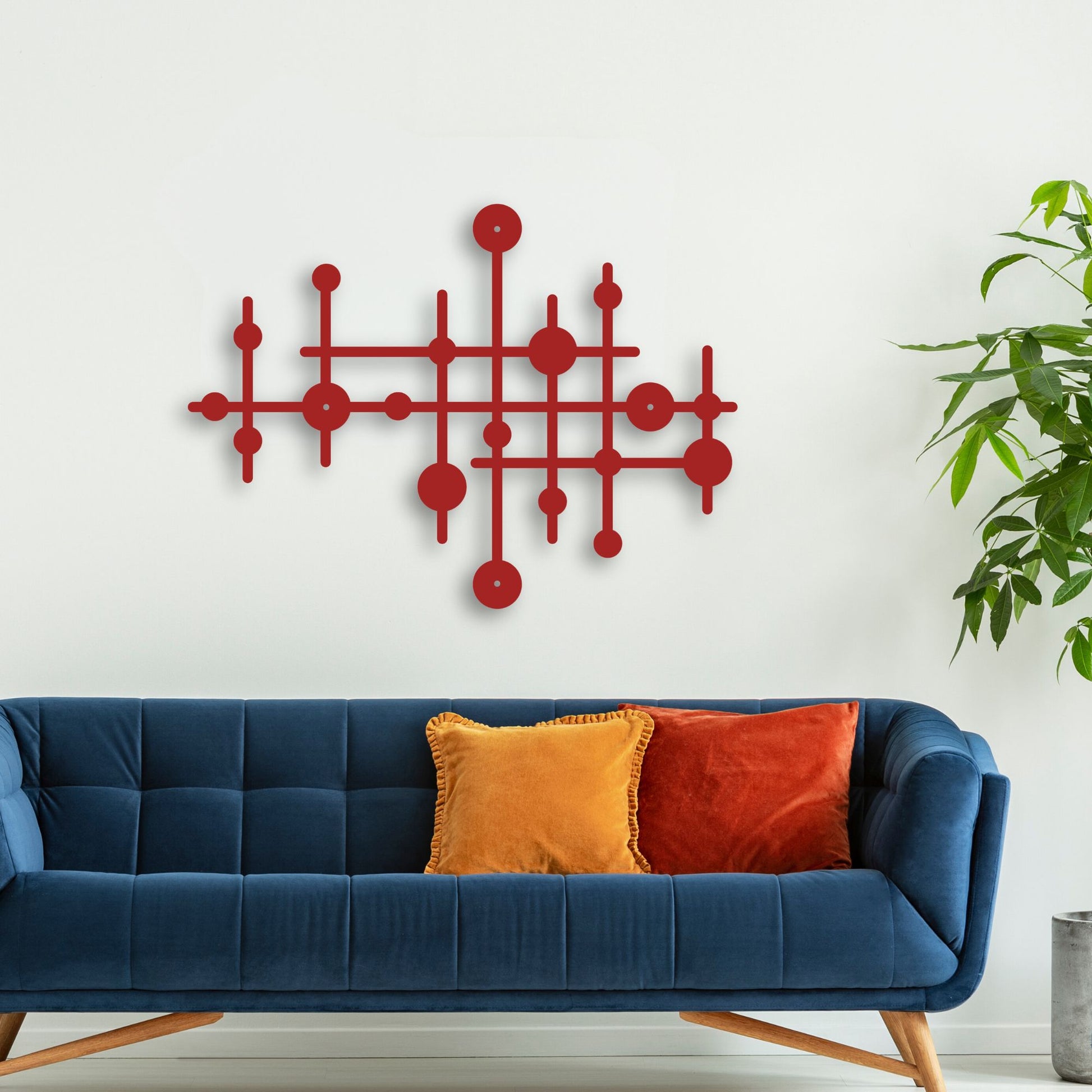 Red geometric wall art above a blue sofa with colorful cushions on a white wall.