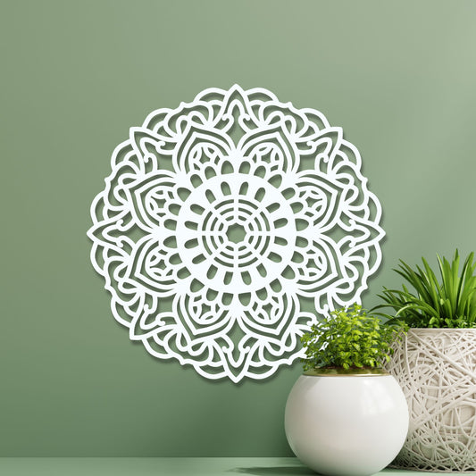 Decorative white mandala wall art on a green wall with plants.