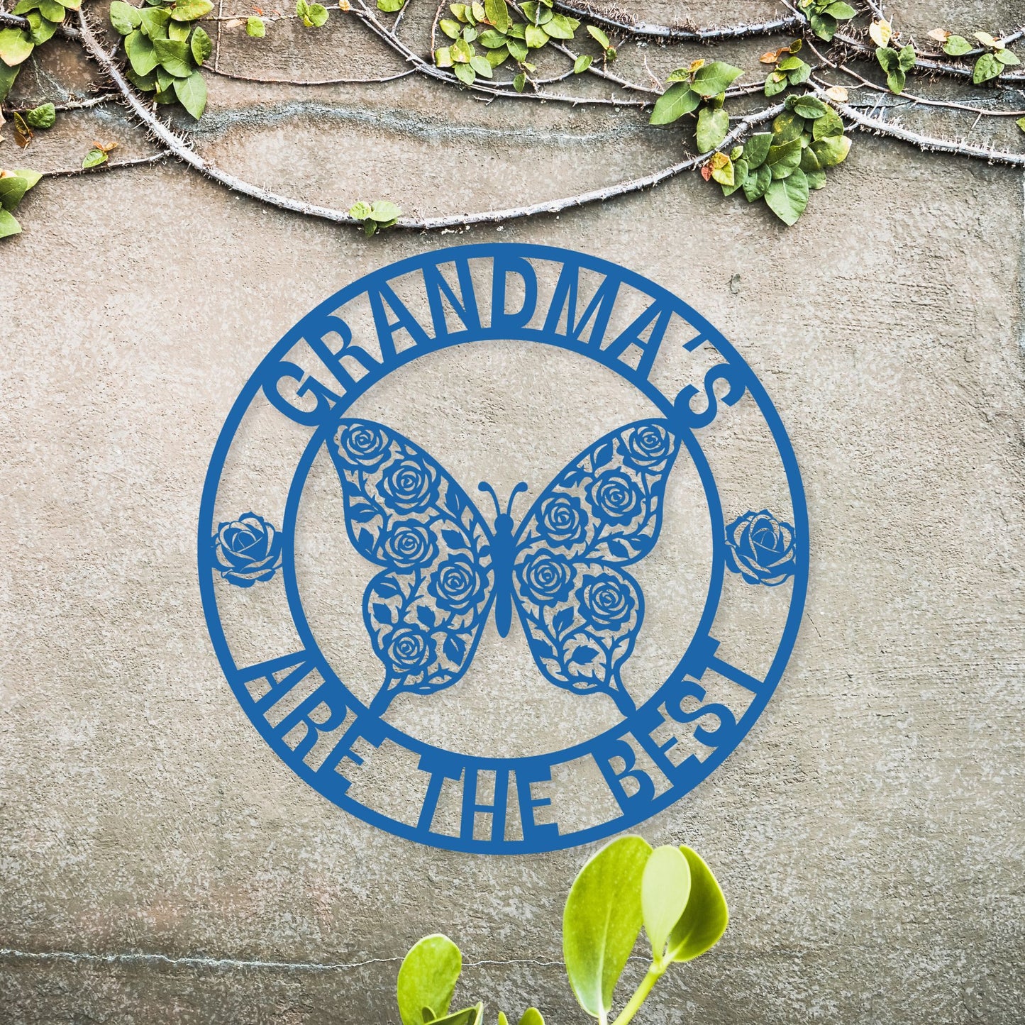 Blue metal sign with butterfly design and 'Grandmas are the best' text on a concrete surface with greenery.