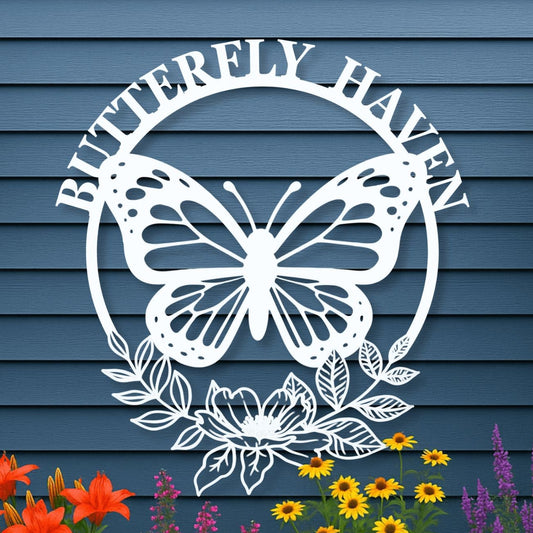 Decorative metal sign with butterfly design and 'Butterfly Haven' text on a blue wooden background with flowers below.
