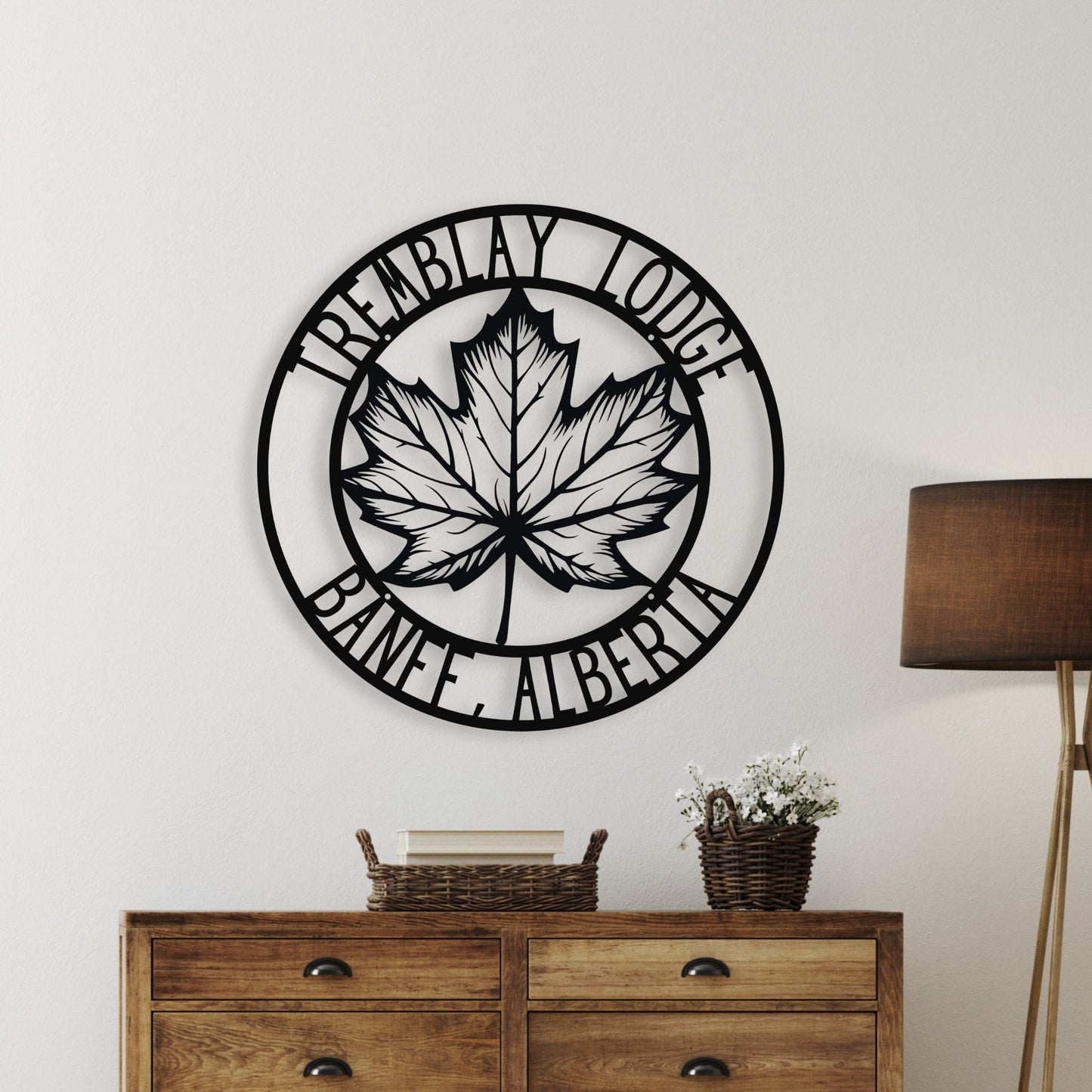 Decorative wall piece with a maple leaf design and text on a white wall above a wooden dresser.