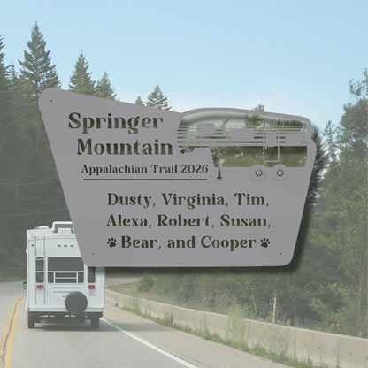White RV on a road with a large sign listing names and 'Springer Mountain Appalachian Trail 2026' in the foreground.