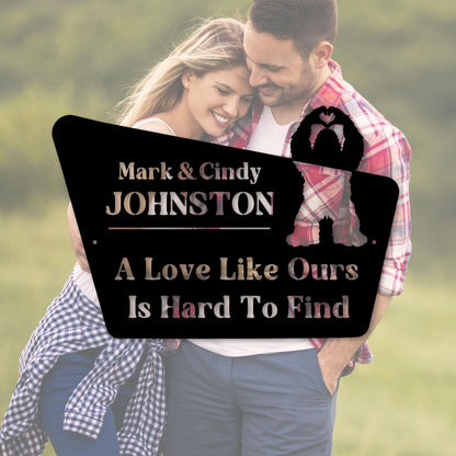 Couple embracing with a personalized sign between them, set against a blurred natural background.