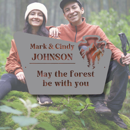 Two people sitting in the forest with a personalized sign between them.