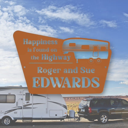 Decorative sign with 'Happiness is found on the Highway' and 'Roger and Sue Edwards' text, with an RV and car in the background.