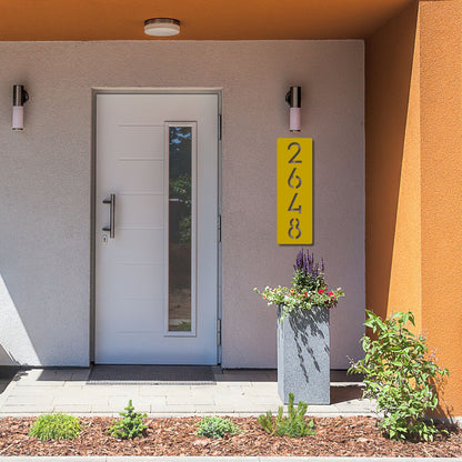 Modern house entrance with a gray door, yellow address sign, and small garden.