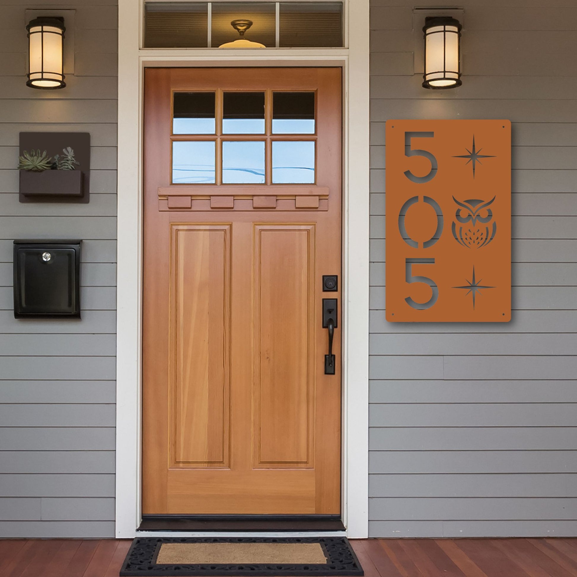 Wooden front door with house numbers and owl design on a gray siding wall.