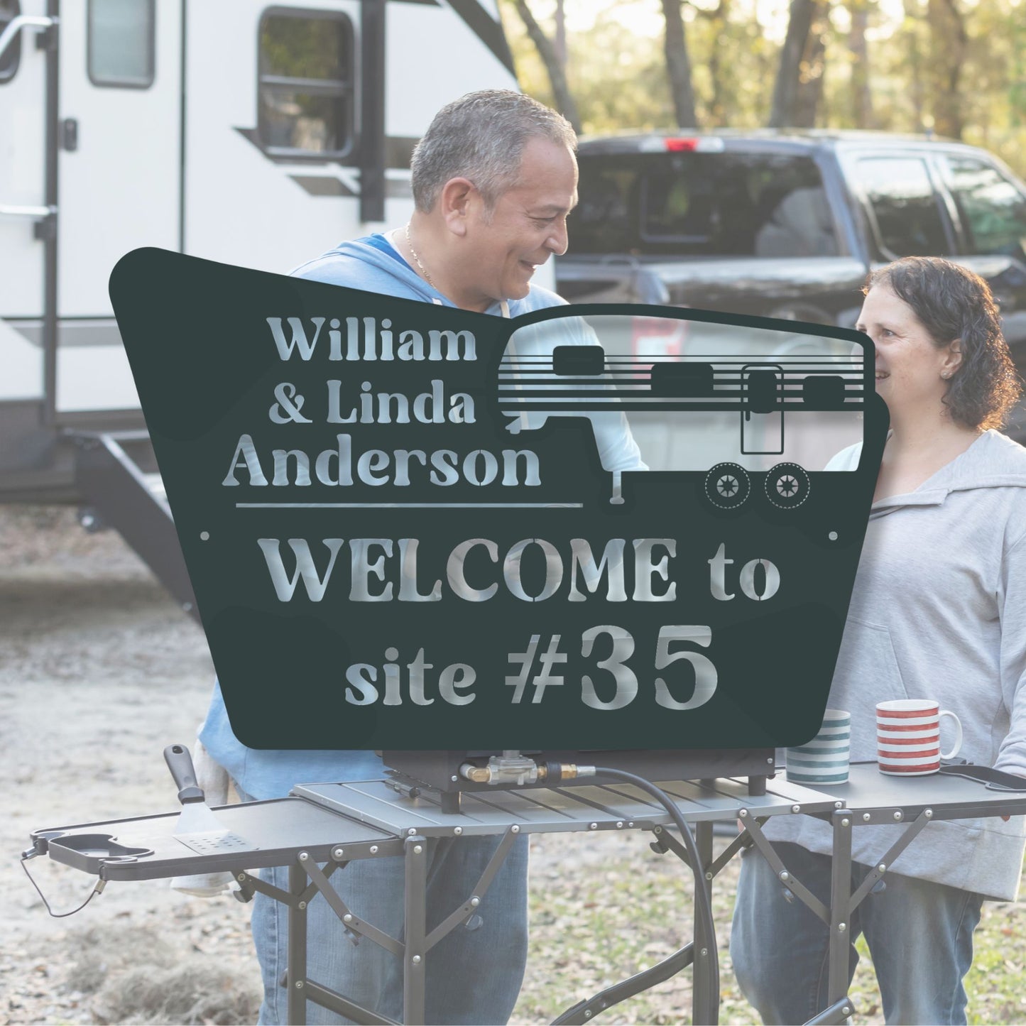 Two people standing next to a personalized camping sign with 'William & Linda Anderson' and 'Welcome to site #35'.