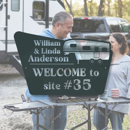 Two people standing next to a personalized camping sign with 'William & Linda Anderson' and 'Welcome to site #35'.