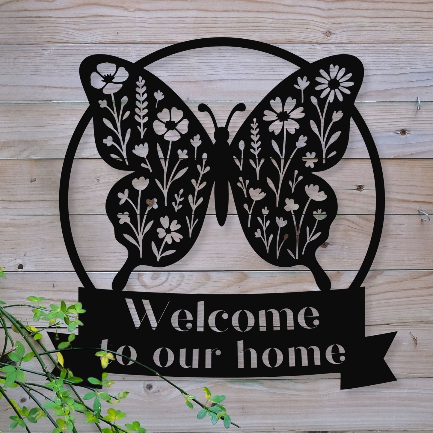 Decorative metal sign with butterfly design and 'Welcome to our home' text on a wooden background.