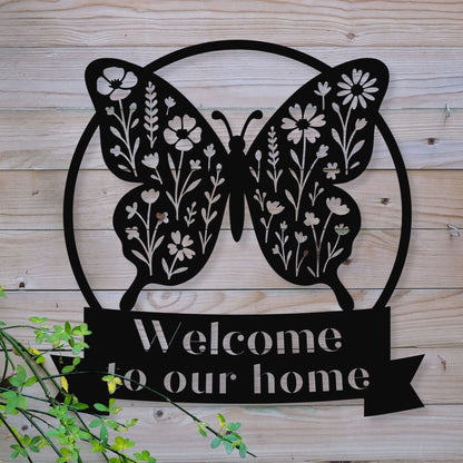 Decorative metal sign with butterfly design and 'Welcome to our home' text on a wooden background.