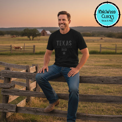 Man sitting on a wooden fence in a field with a sunset, wearing a 'Texas Dad' t-shirt.