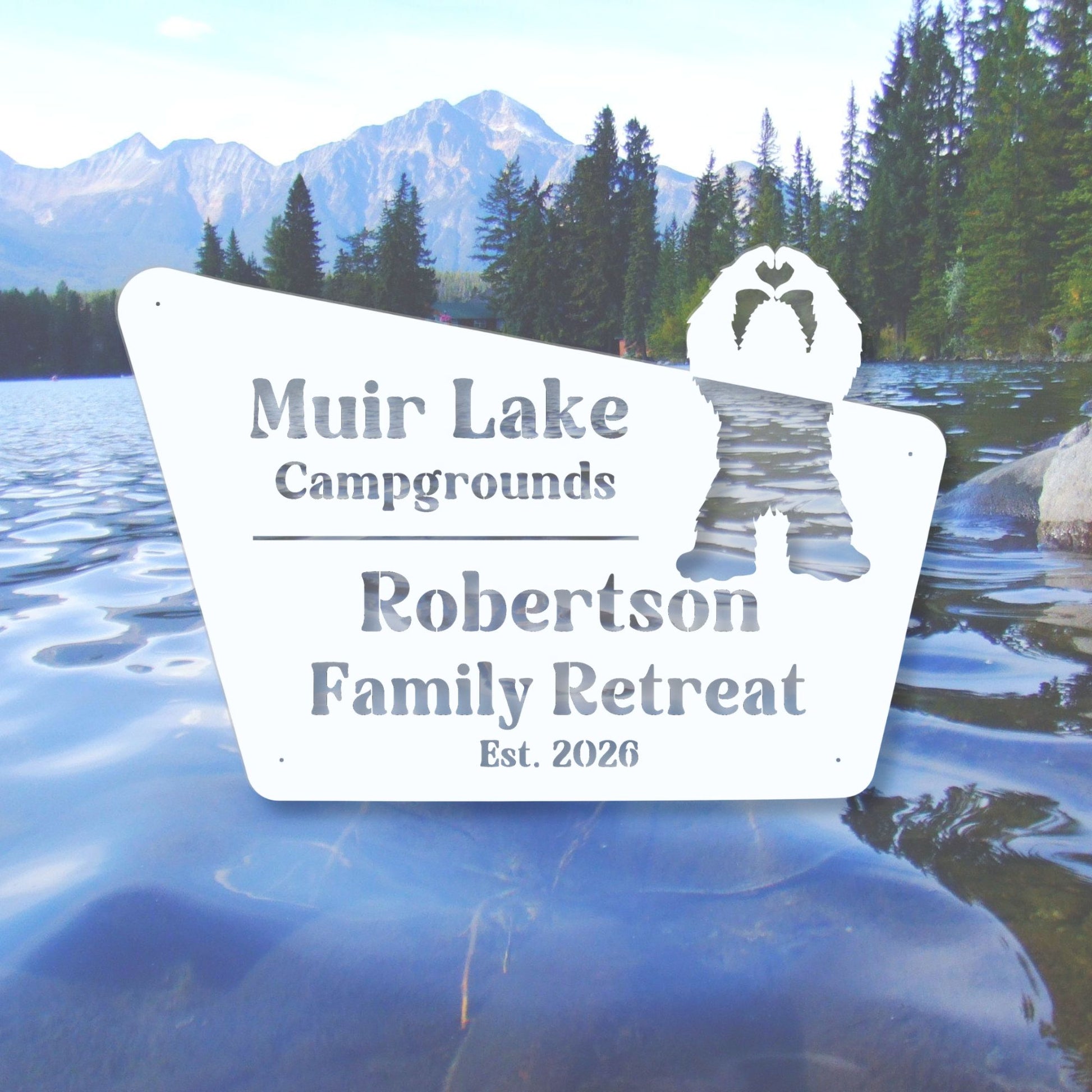 Sign for Muir Lake Campgrounds Robertson Family Retreat with a scenic background of a lake and mountains.
