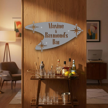 Decorative sign on a wooden wall with barware and bottles on a cart below.