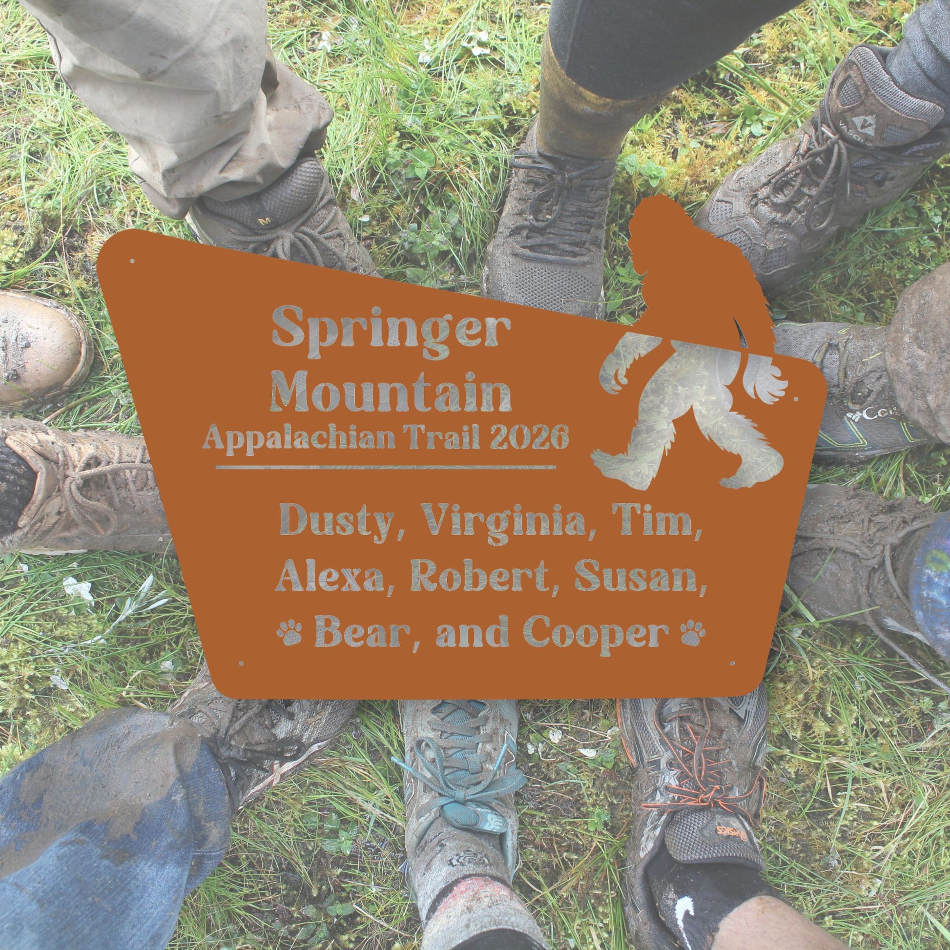 Person wearing hiking boots with a 'Springer Mountain Appalachian Trail 2020' sign featuring a silhouette of a bear.