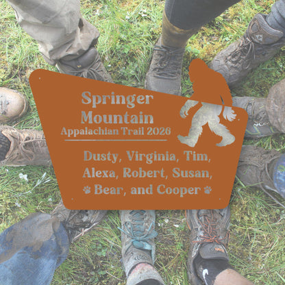 Person wearing hiking boots with a 'Springer Mountain Appalachian Trail 2020' sign featuring a silhouette of a bear.