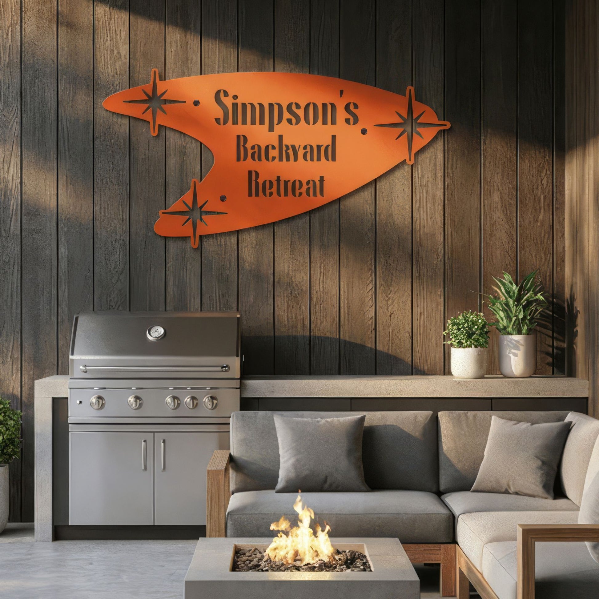 Outdoor living space with a grill, sofa, and fire pit against a wooden wall with a decorative sign.