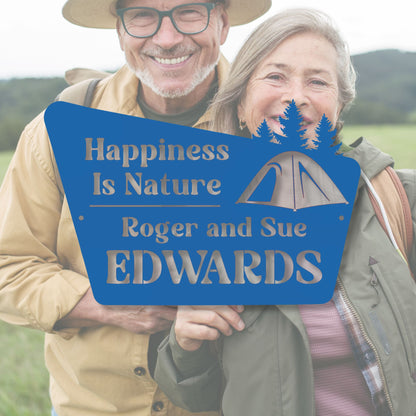 Two people standing outdoors with a blue sign that reads 'Happiness Is Nature' and 'Roger and Sue Edwards'.