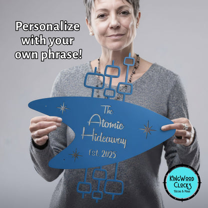 Woman holding a blue sign with 'The Atomic Hideaway' text, promotional image for Kingwood Clocks.