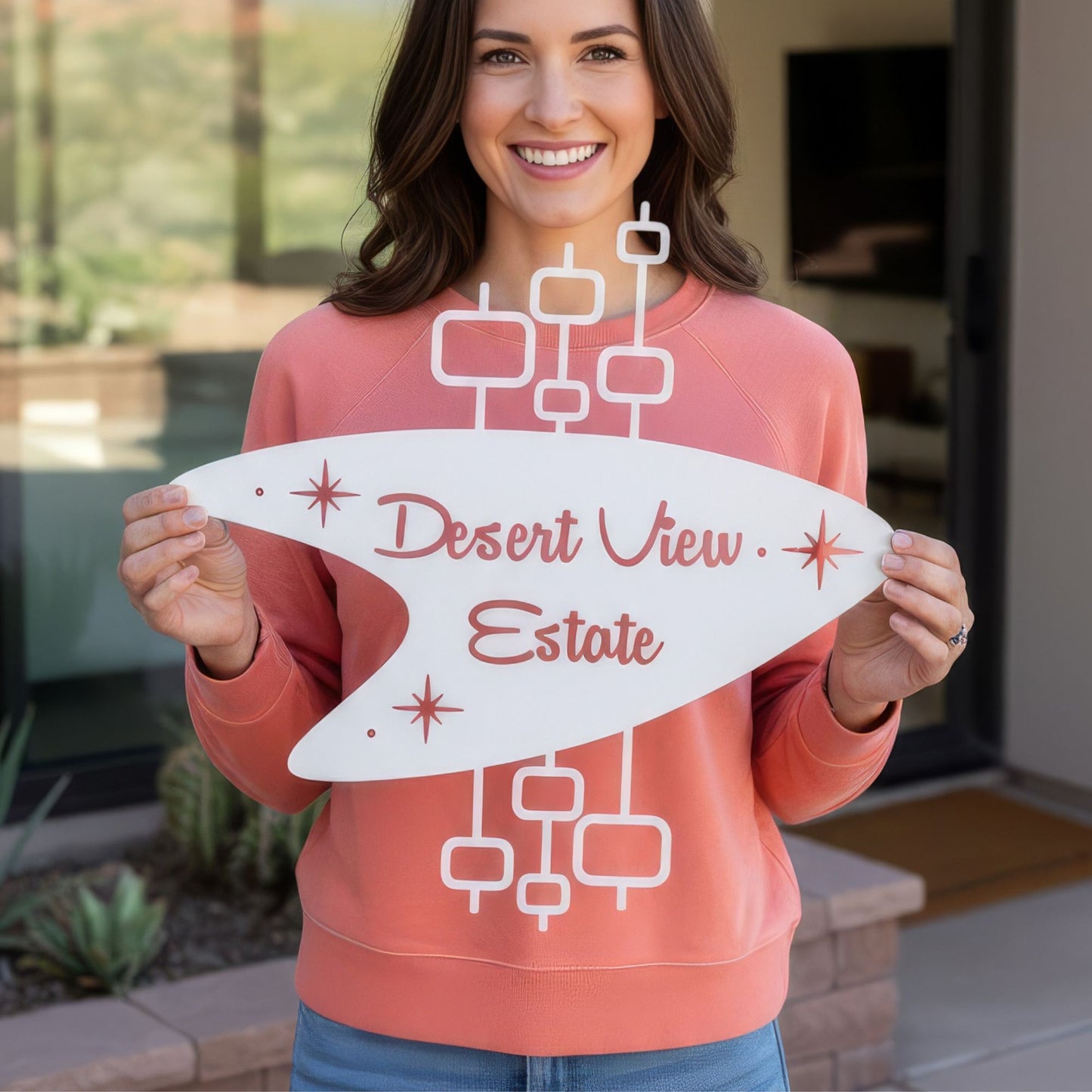 Woman holding a 'Desert View Estate' sign in front of a house.
