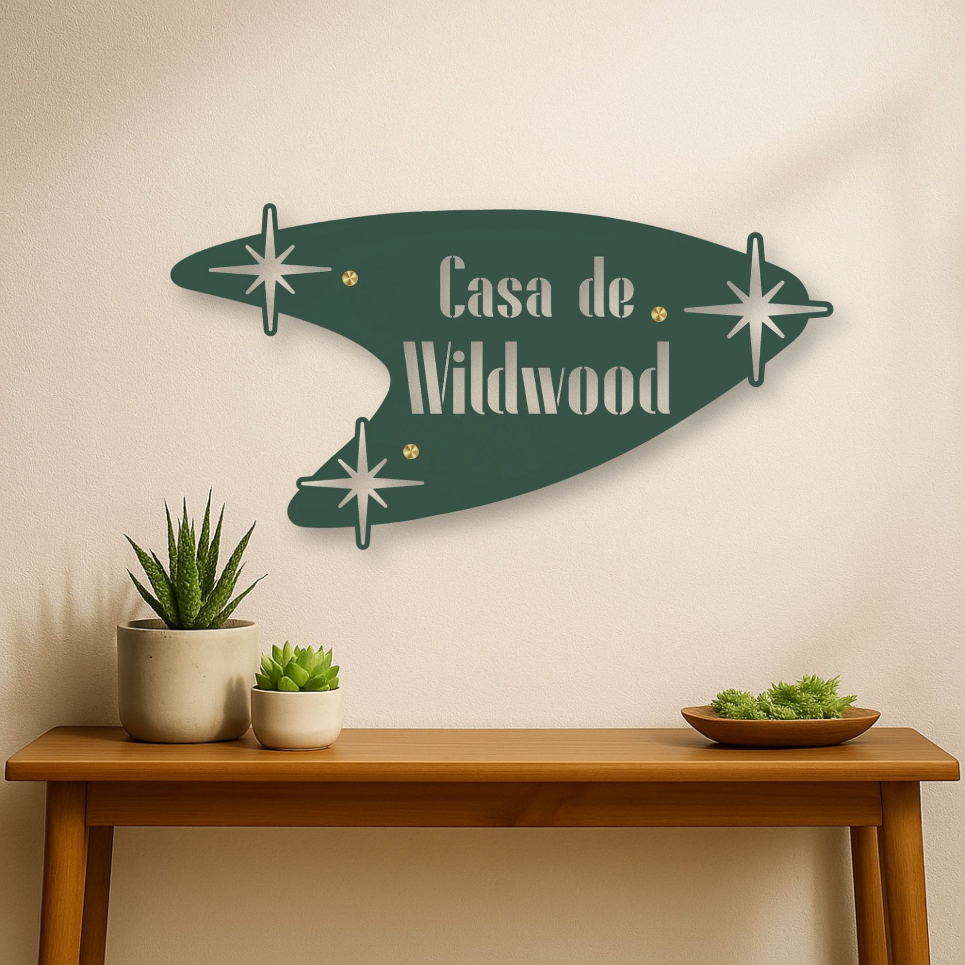 Decorative wall sign with 'Casa de Wildwood' text on a beige wall above a wooden table with plants.