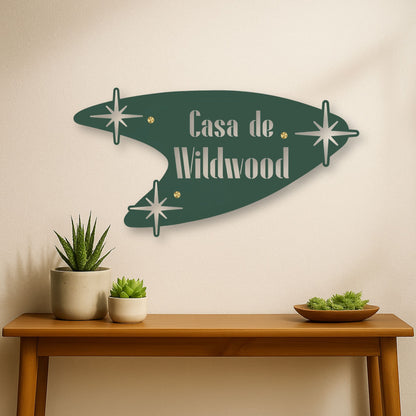 Decorative wall sign with 'Casa de Wildwood' text on a beige wall above a wooden table with plants.
