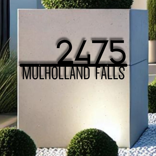 Modern house number sign '2475 Mulholland Falls' on a concrete block with greenery.