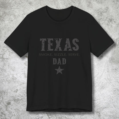 Black t-shirt with 'Texas Smoke, Sizzle, Serve Dad' text on a textured gray background