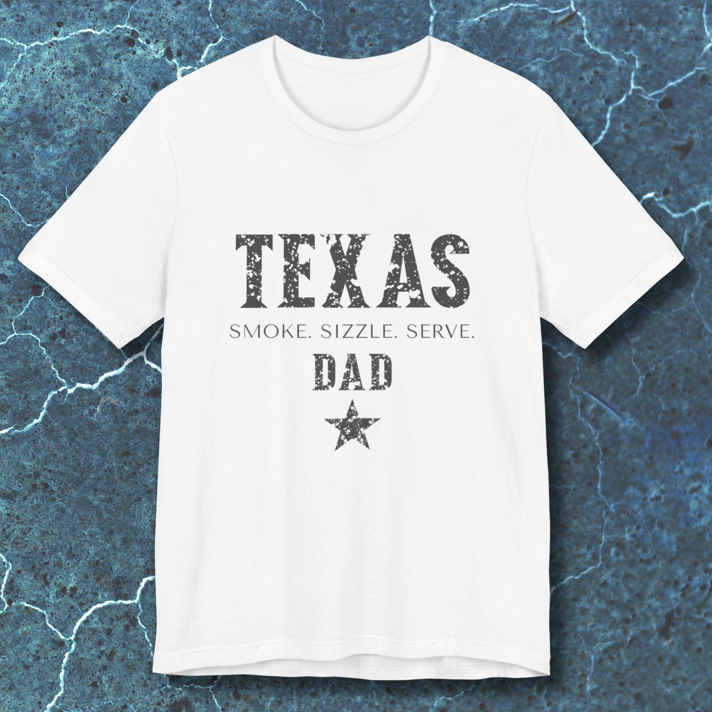 White t-shirt with 'TEXAS SMOKE. SIZZLE. SERVE. DAD' text on a textured blue background